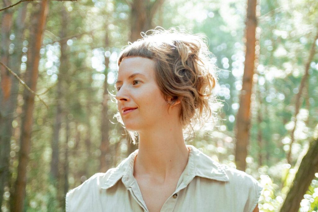 Anne in the woods with her eyes closed, surrounded by nature's beauty.