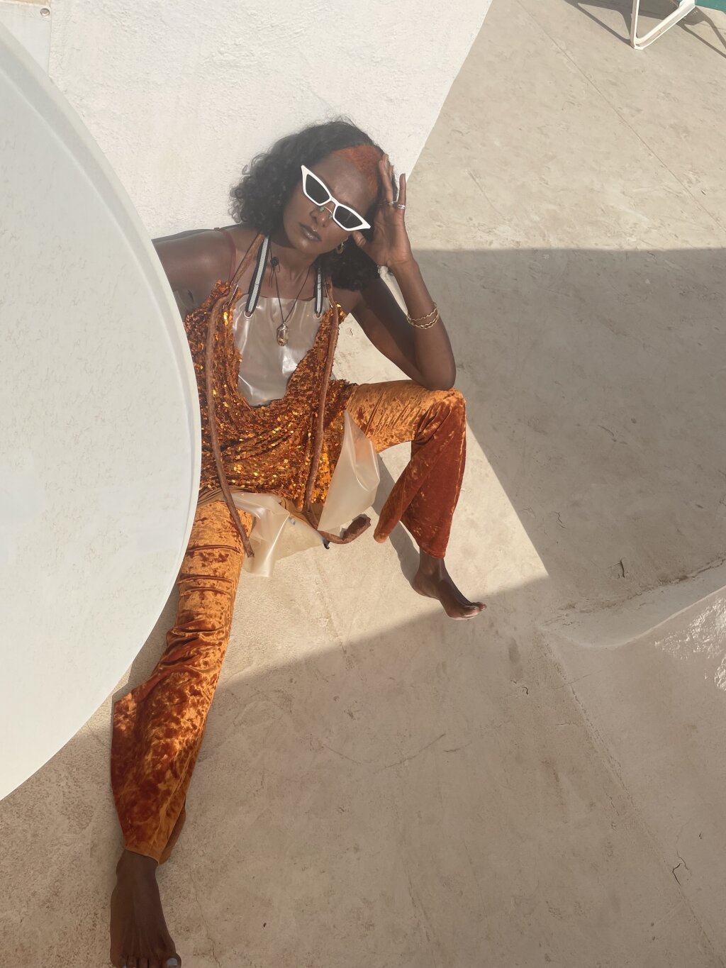 A woman in an orange outfit sits on the floor of a rooftop.