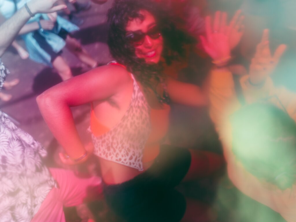 A blurry photo of a woman dancing happily with more people around her.