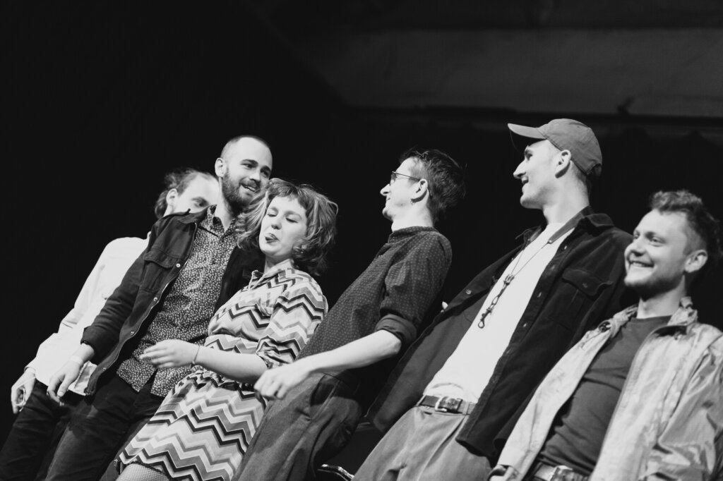 A diverse group of people standing together on stage, smiling and looking at the audience.