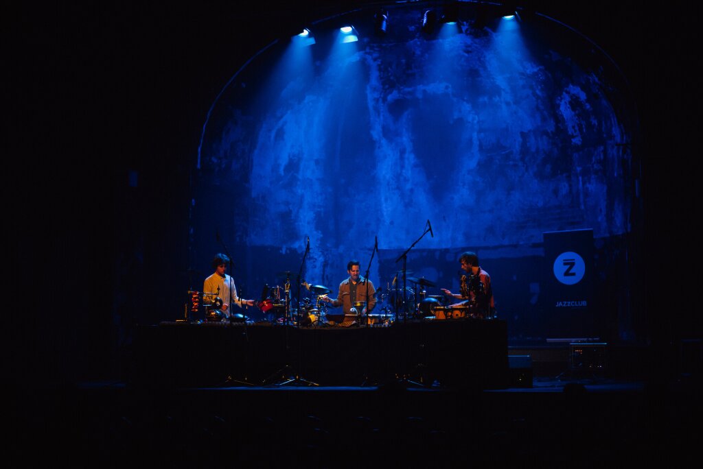 The three drummers of Popp Drum Trio on a stage in blue light.