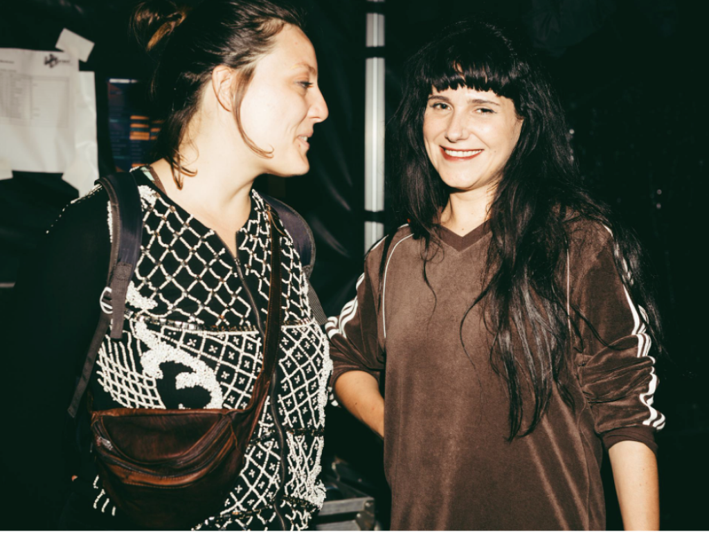 two women, one is smiling at the camera, the other is looking at the woman.