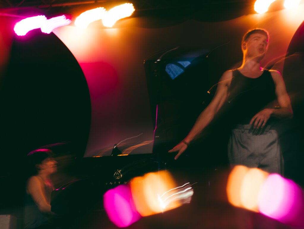 A non-binary person playing the Steinway piano while a man is singing.