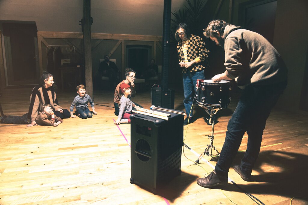 People of different ages sitting around a drum set, played by an artist.